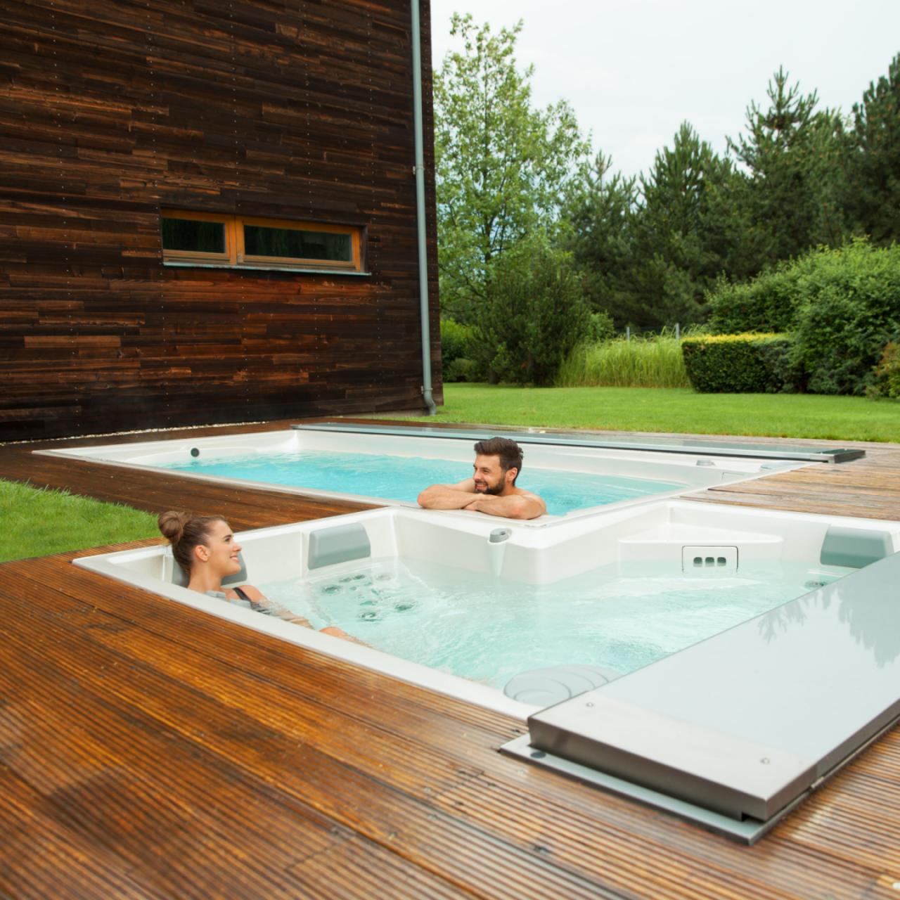 Pár relaxující ve venkovních lázních USSPA a bazénech swim spa instalovaných na dřevěné terase