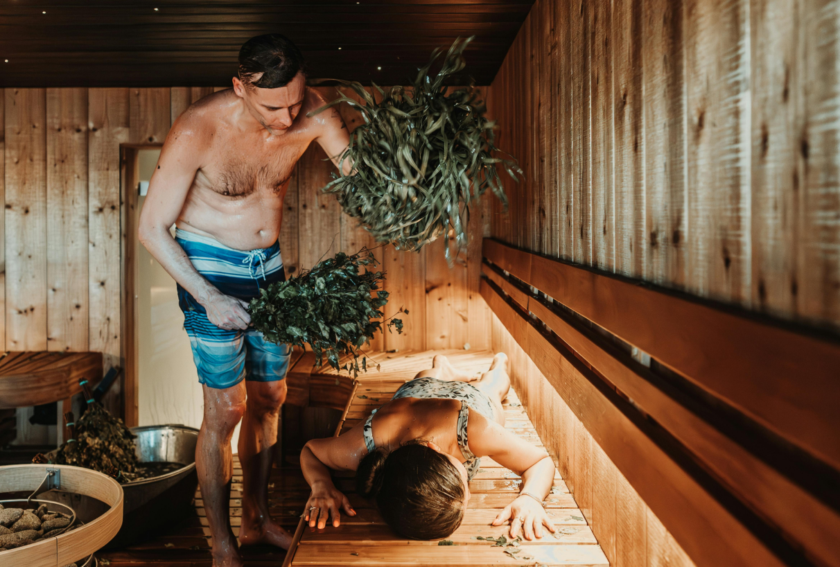Muž v sauně bije ženu březovou metličkou – tradiční saunový rituál pro relaxaci